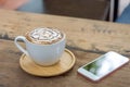 Latte art coffee cup with wooden saucer and smartphone on table