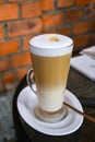 Latte Coffee macchiato in tall glasses with table settings in street cafe. Red brick wall background Royalty Free Stock Photo