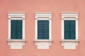 Three green wooden window with shutters in a white frame on pink wall Royalty Free Stock Photo