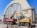 A wheeled excavator loads a dump truck with soil near Riga Central market pavilion