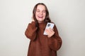 Laughing adorable Caucasian woman wearing brown jumper standing isolated over gray background scrolling online chatting on