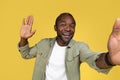 Laughing adult african american man in casual waving hand at camera and taking selfie for blog