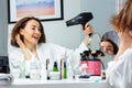 Laughing adult woman in housecoat holding hairdryer dry hair