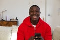 Laughing african american man sitting on couch at home using on smartphone Royalty Free Stock Photo