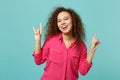 Laughing african girl in pink casual clothes showing horns up depicting heavy metal rock sign isolated on blue turquoise Royalty Free Stock Photo