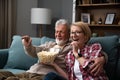 Laughing aged couple, man and woman watching tv, comedy show or movie and eating popcorn snack, sitting on cozy couch at home, Royalty Free Stock Photo