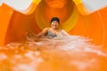 Laughing amused elderly caucasian female pensioner in black hair cap sliding on an orange water slide