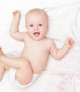 Laughing baby in diaper laying on the white bed