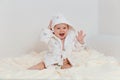 Laughing baby girl in a Terry robe and diaper sitting on the bed after bathing. an eight-month-old Caucasian kid Royalty Free Stock Photo