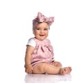 Cute smiling infant baby girl toddler in polka-dot dress and headband with bow sits on the white floor Royalty Free Stock Photo