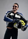 Laughing bearded man biker motocross race winner in motorcycle leather jacket and gloves stands holding his helmet Royalty Free Stock Photo