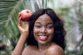 Laughing black woman with fresh red pomegranate. Photo of pleasant afro woman with nude makeup on tropic palms Royalty Free Stock Photo