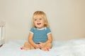 Laughing blond toddler boy sit on the bed in nursery