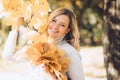 Laughing blond woman, holding bunch of golden foliage yellow leaves maples in two hands near tree, decorate blur. Close Royalty Free Stock Photo