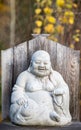 The Laughing Buddha, Budai, with his cloth sack stone sculpture with yellow fall colors in the background Royalty Free Stock Photo