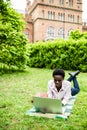 Surf in internet. Young afro american student lying on grass taking notes on campus at college Royalty Free Stock Photo