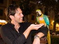 laughing caucasian handsome man in black shirt holds a parrot and feeds it