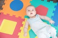 Laughing child on a colored rubber mat puzzle for playing foam with geometric figures
