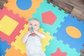 Laughing child on a colored rubber mat puzzle for playing foam with geometric figures