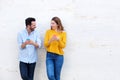 Laughing couple standing by white wall holding mobile phones Royalty Free Stock Photo