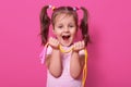 Laughing cute girl wears rose t hirt, stands isolated over pink background, hold bright skipping rope in hands. Happy child with