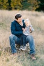 Laughing dad hugging little girl sliding off his knees on the lawn