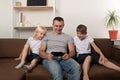 Laughing dad and two sons are sitting on couch and watching a video on phone. Happy family Royalty Free Stock Photo