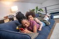 Laughing darkskinned woman and little daughter lying on sofa