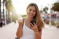 Laughing excited young woman watching her smartphone celebrating outdoor raising her fist up in exultation