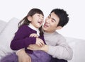 Laughing father tickling daughter and bonding on the sofa, studio shot