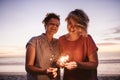 Laughing female friends playing with sparklers during a beach sunset Royalty Free Stock Photo