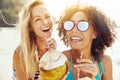 Laughing female friends walking along a beach drinking from coco Royalty Free Stock Photo