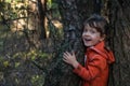 Laughing five-years-old girl stands between two trees in autumn forest.