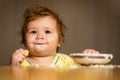 Laughing funny baby with dirty food face. Happy child spoon eats itself.