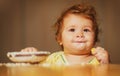 Laughing funny baby with dirty food face. Happy child spoon eats itself. Royalty Free Stock Photo