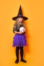 Laughing funny child girl in a witch costume in halloween on orange background Royalty Free Stock Photo