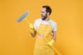 Laughing funny young man househusband in apron rubber gloves hold in hands broom while doing housework isolated on