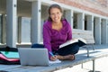 Laughing german female student learning with book and computer in front of school building Royalty Free Stock Photo