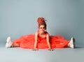 Laughing girl with colorful dreadlocks in coral big dress, sneakers, sunglasses sits on floor legs wide apart reaching Royalty Free Stock Photo