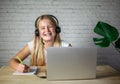 Laughing girl in headphones using laptop and making notes in her notebook, e-learing, children using technology Royalty Free Stock Photo