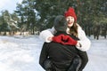 Laughing girl keeps hands in heart shape sign sitting on her guy hands. Young loving couple in winter forest. Sunny day