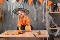 Laughing girl prepares a pumpkin jack-o-lantern for Halloween carnival. Witch hat and makeup on the child. take out the