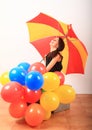 Laughing girl with red and yellow umbrella behind inflating balloons Royalty Free Stock Photo