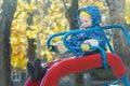 Laughing girl in warm hooded jacket sliding down red plastic playground slide at yellow autumn tree leaves background