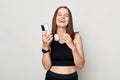 Laughing happy cheerful woman wearing black top standing isolated over white background holding cell phone looking at camera Royalty Free Stock Photo