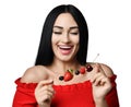 Happy smiling brunette woman in red off shoulder dress holding a small skewers with berries isolated on white.