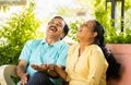 Laughing indian senior couple talking each other while sitting at park - concept of relaxation, conversation and Royalty Free Stock Photo