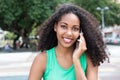 Laughing latin woman with curly hair and green shirt at phone in Royalty Free Stock Photo