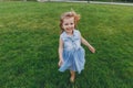 Laughing little cute child baby girl in denim dress walking and running, have fun on green grass lawn in park. Mother Royalty Free Stock Photo