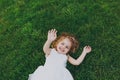 Laughing little cute child baby girl in light dress lie on green grass lawn, showing palm on camera in park. Mother Royalty Free Stock Photo